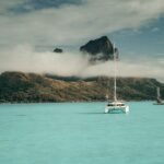 white boat on sea near mountain under white clouds during daytime