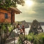 man in red t-shirt sitting on brown wooden ladder near green trees during daytime