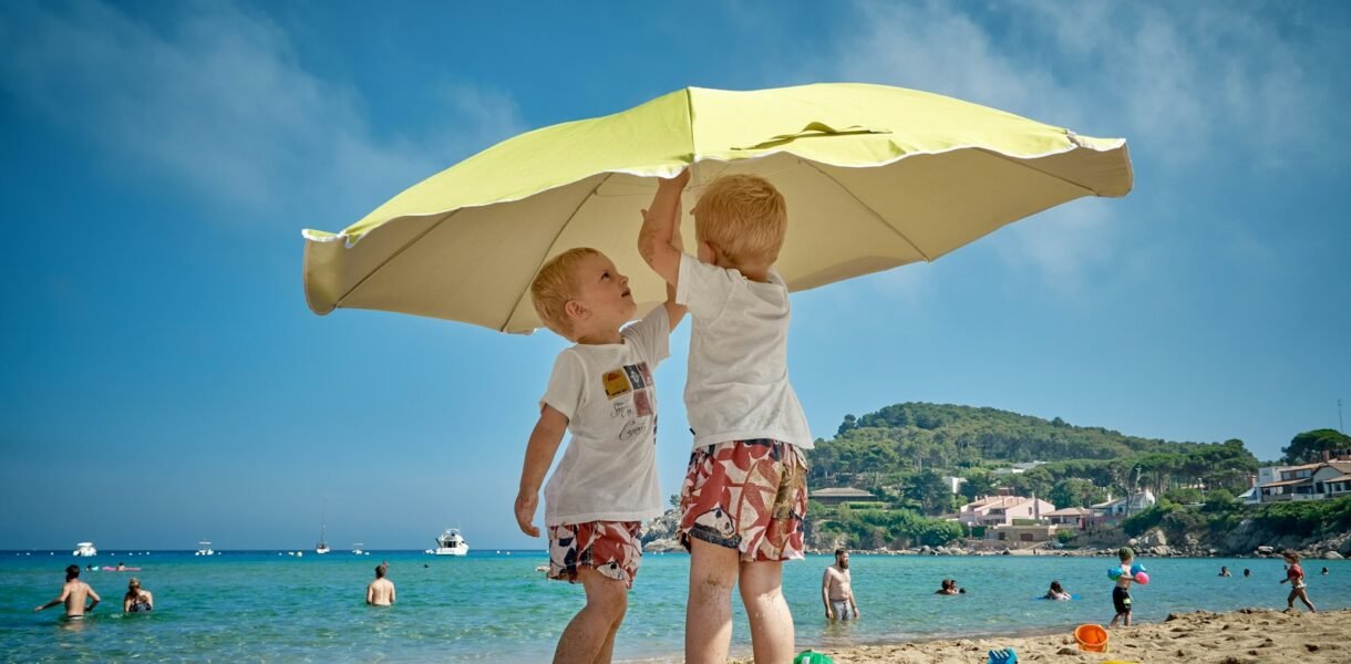 two children playing under umbrella on seashore