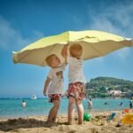 two children playing under umbrella on seashore