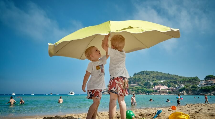 two children playing under umbrella on seashore